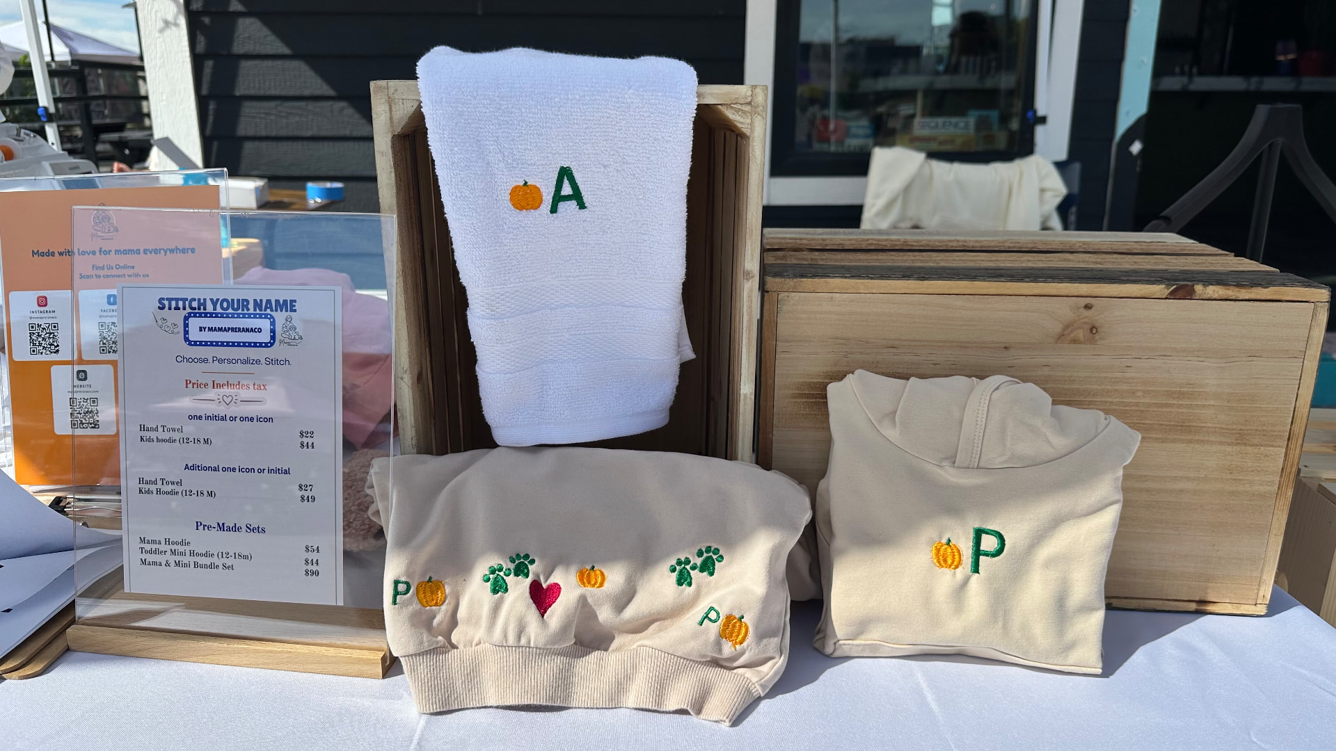 Finished embroidered apparel and towels on display at a MamaPreranaCo live embroidery pop-up