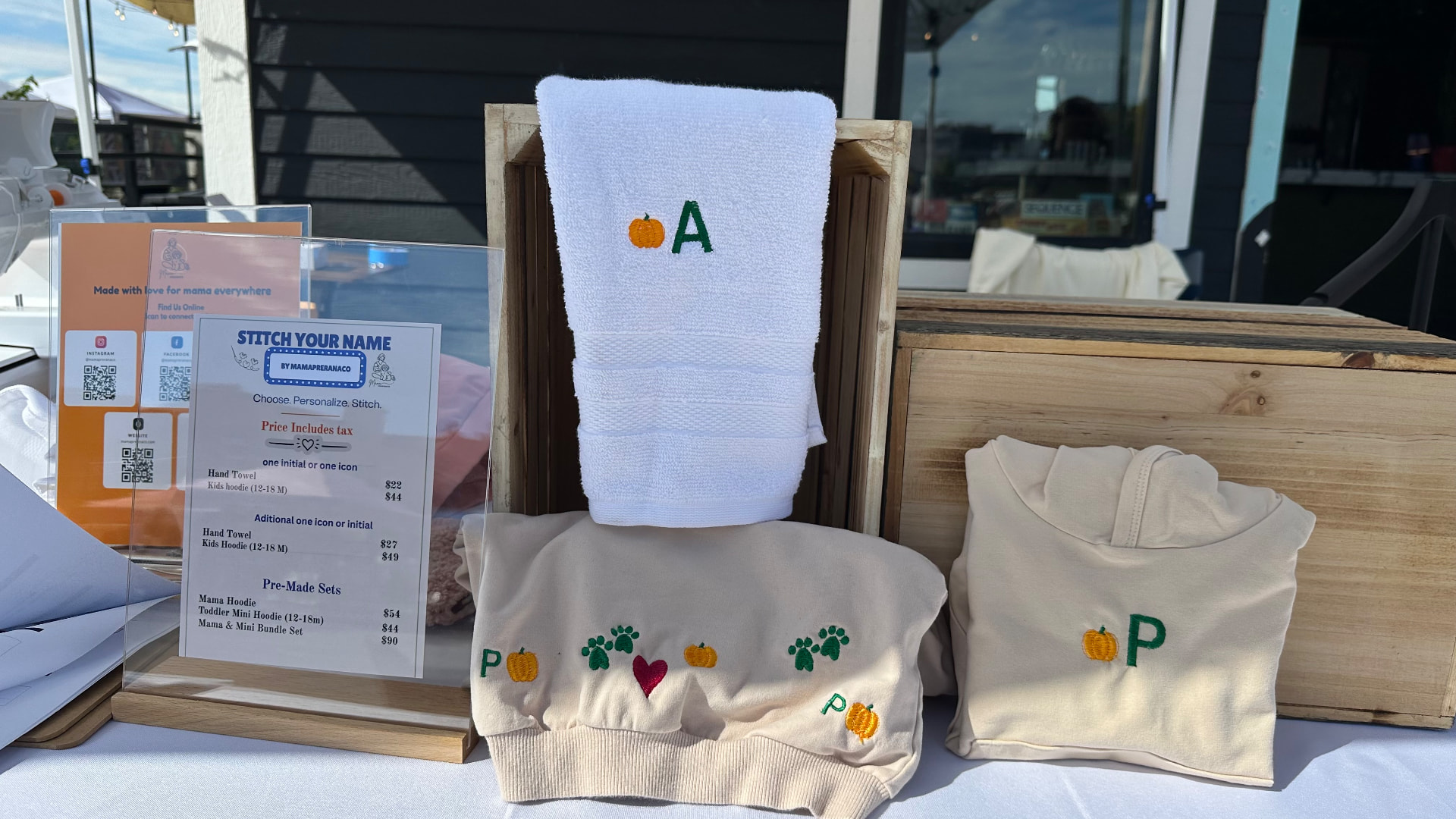 Live embroidery stitch menu and pricing sign at a MamaPreranaCo event booth